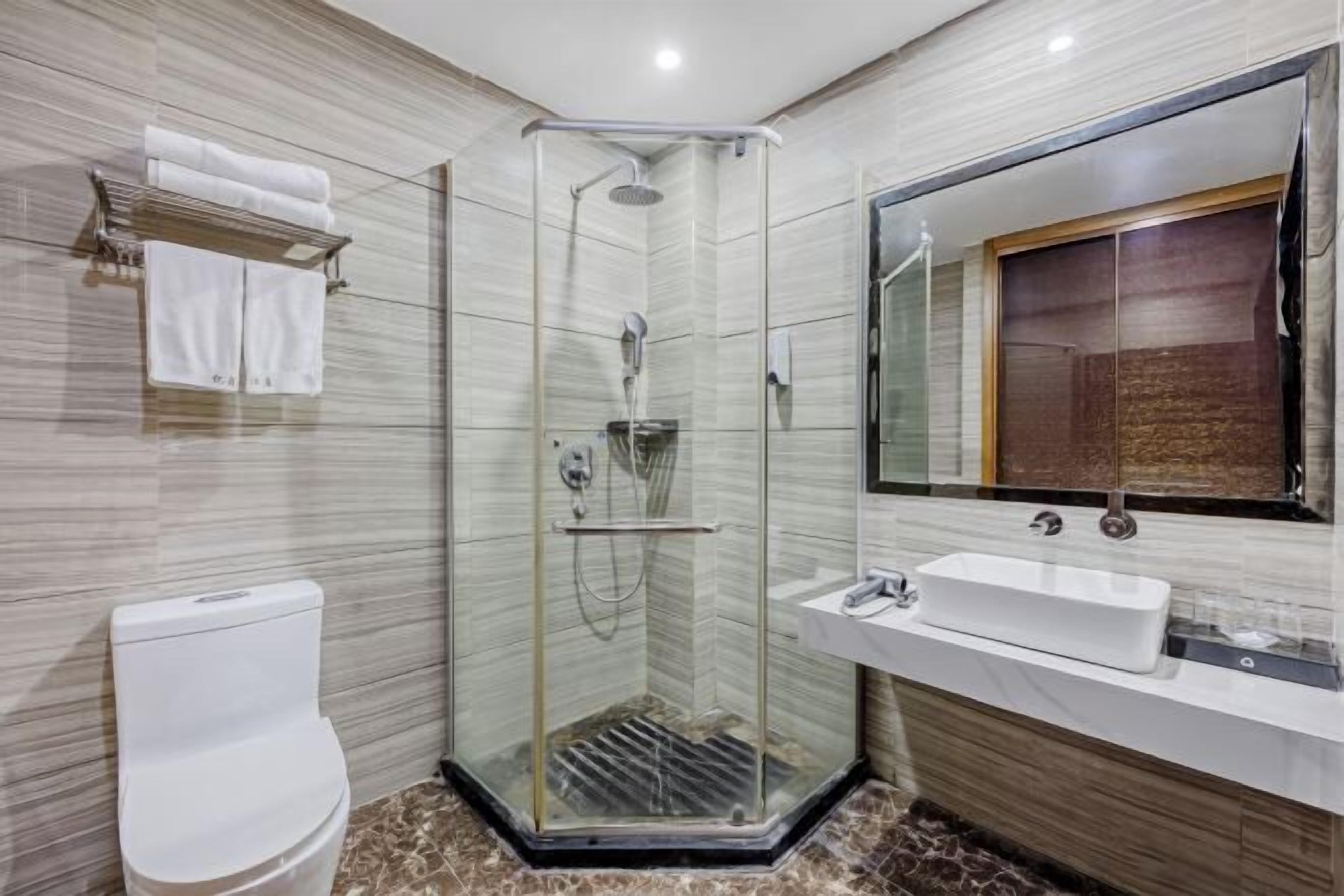 Uma casa de banho moderna com chuveiro em cabine de vidro, sanita branca, lavatório e espelho grande.