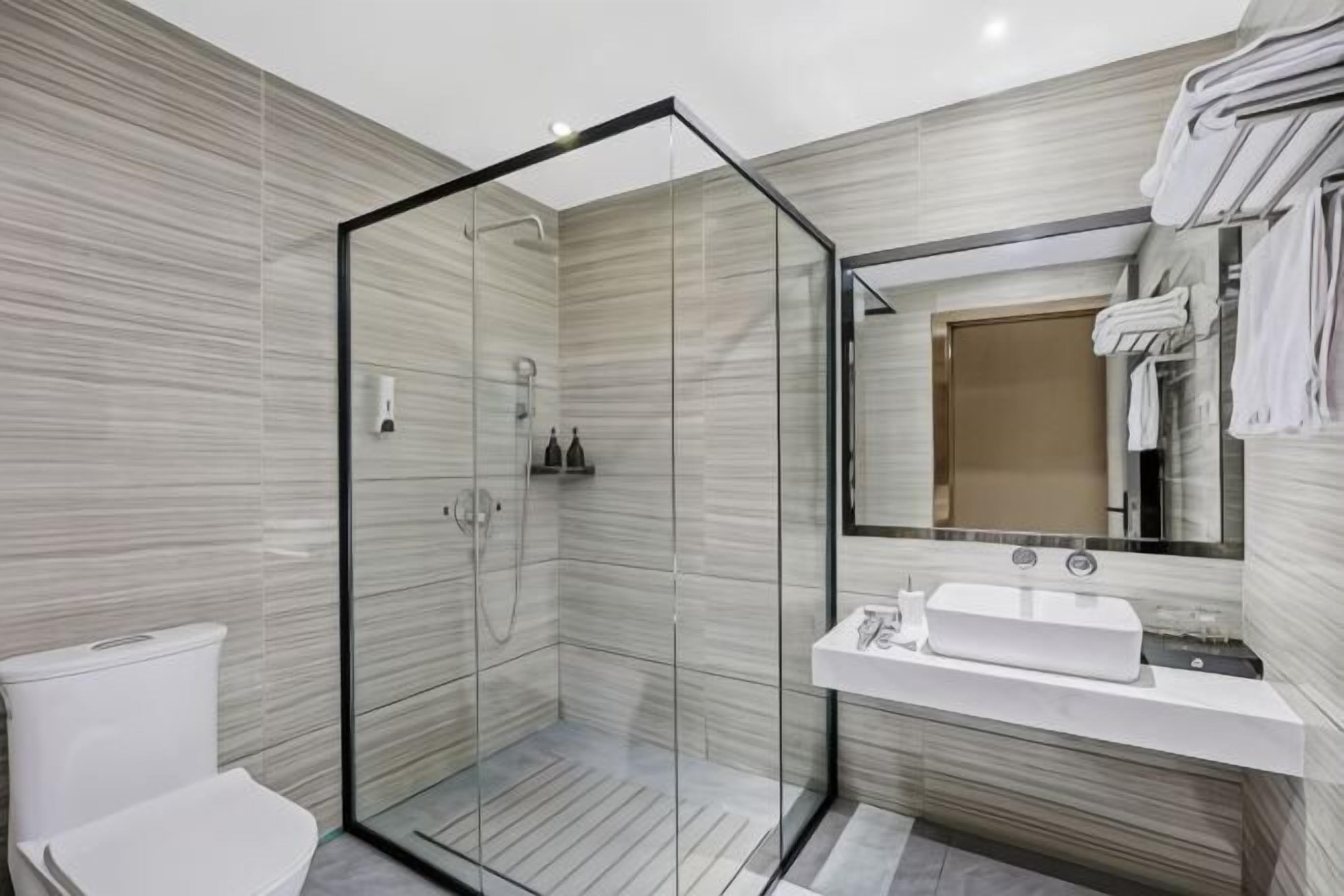 Un baño moderno con ducha de vidrio, lavamanos blanco y un espejo grande.