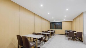 A conference room with multiple tables and chairs, beige walls, and a large window. - Anqing Yixin Hotel (Anqing)
