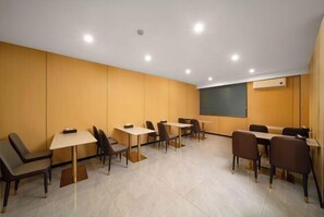 A conference room with multiple tables and chairs, a projector screen, and recessed ceiling lights. - Anqing Yixin Hotel (Anqing)