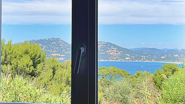 Blick durch ein Fenster auf bewölkten Himmel, entfernte Hügel und ein Gewässer.
