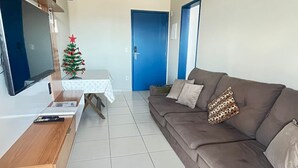 A living room with a brown sofa, a TV, a small Christmas tree, and a door. - Apartment in Praia Grande - Gourmet balcony with sea view - Air conditioning - Parking space (Praia Grande)