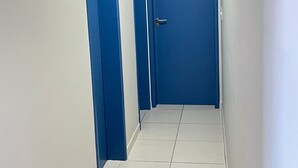 A narrow hallway with white tiled floors and blue doors. - Apartment in Praia Grande - Gourmet balcony with sea view - Air conditioning - Parking space (Praia Grande)