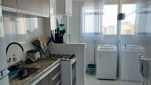 A compact kitchen with white cabinets, a granite countertop, a built-in oven, and a refrigerator. - Apartment in Praia Grande - Gourmet balcony with sea view - Air conditioning - Parking space (Praia Grande)