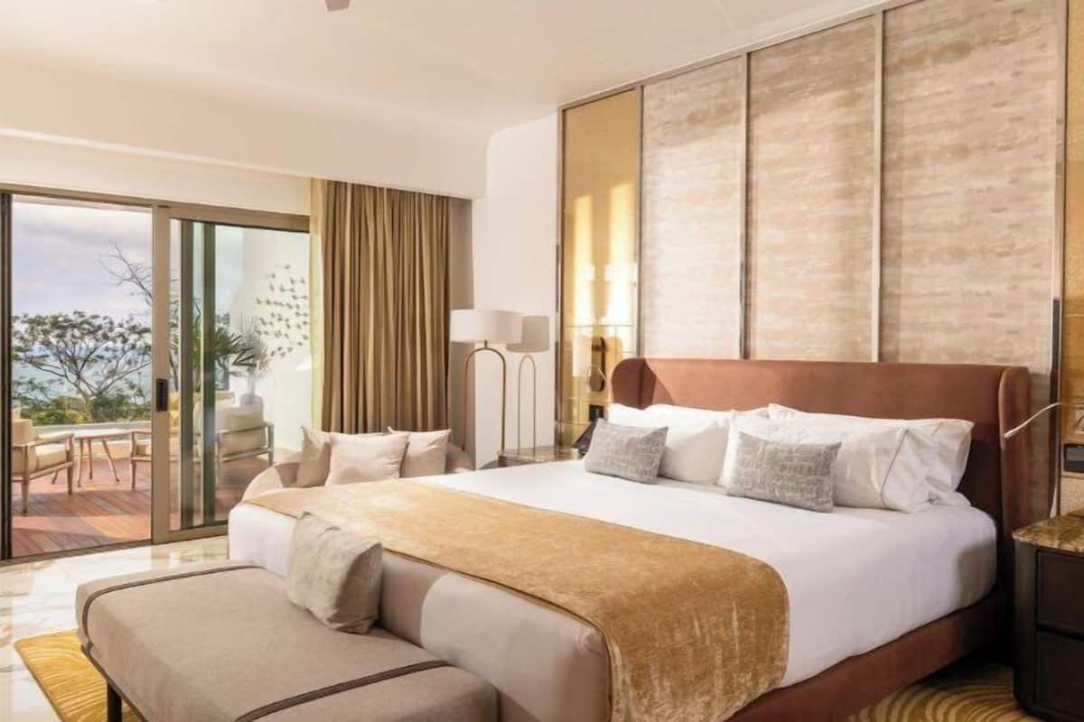 A hotel room with a large bed, a desk, a chair, a lamp, and a view of the outdoors.