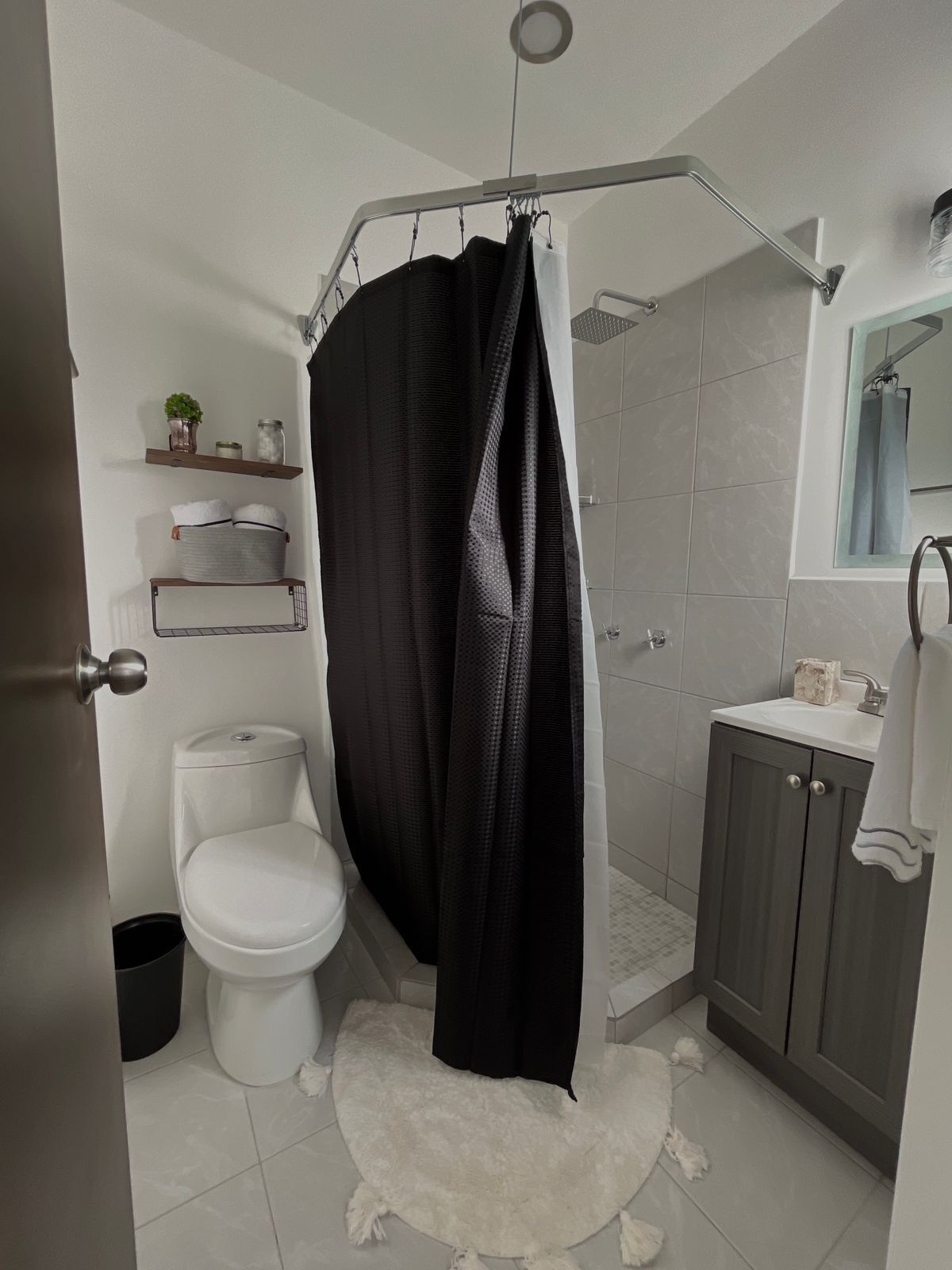 A modern bathroom with a toilet, shower, and sink. There are shelves with toiletries and a mirror above the sink.