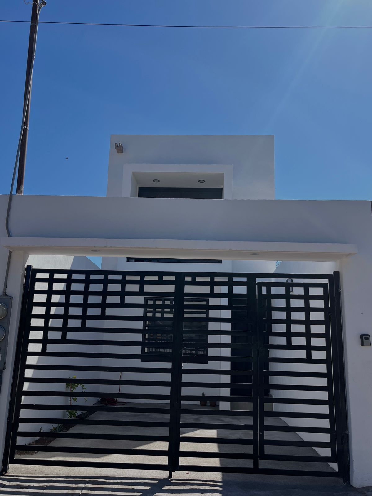 A modern building with a white facade, a black metal gate, and a small window above the gate.