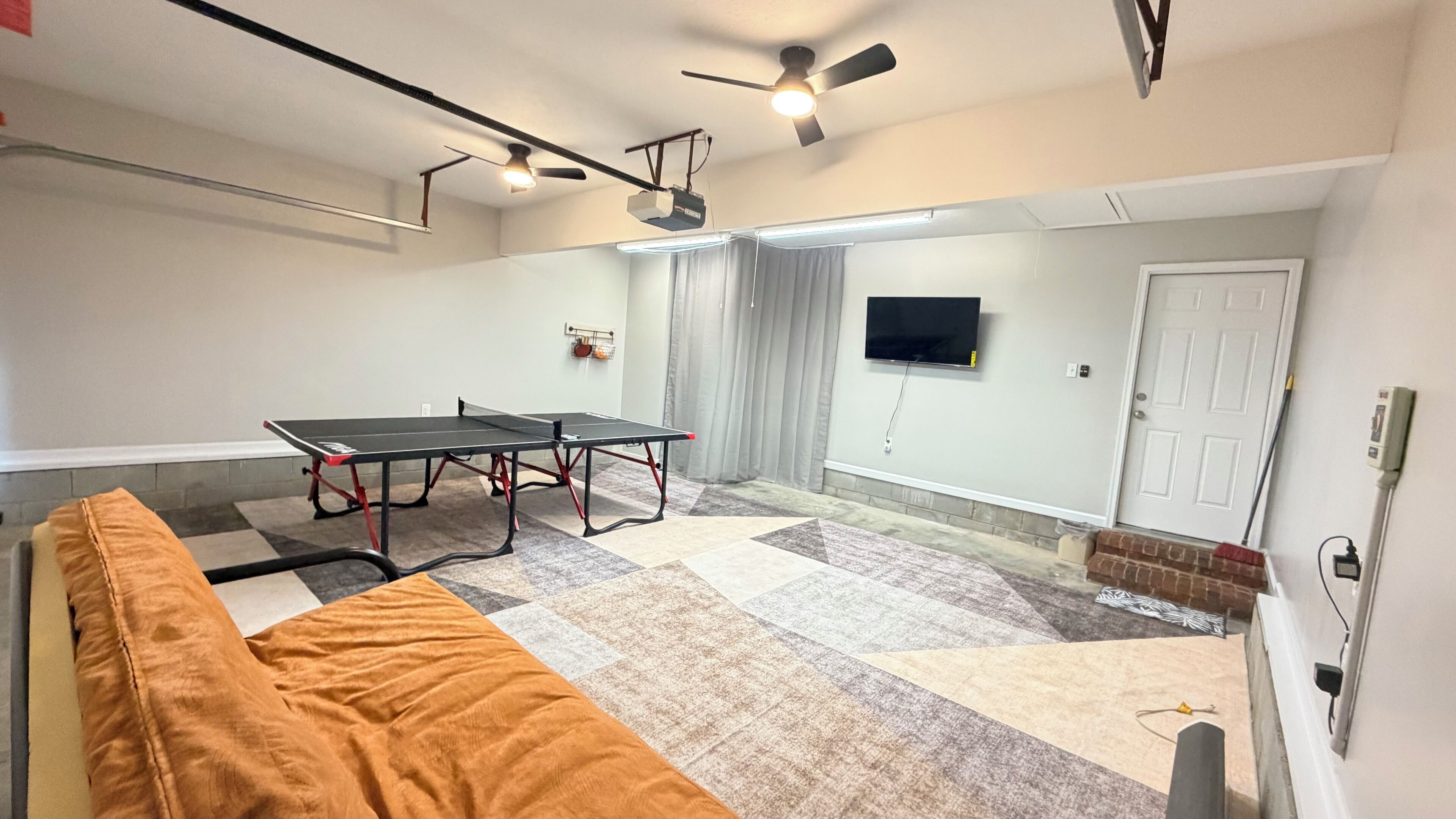 Een kamer met een tafeltennistafel, een plafondventilator, een televisie en een deur.