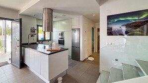 A modern kitchen with a central island, stainless steel appliances, and a dining area with a glass table. - Gorgeous home in Rojales (Rojales)