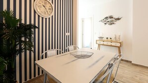 A dining area with a striped wall, a round clock, a table with chairs, and a decorative wall piece. - Sea & Sun Apartment II (Nazaré)