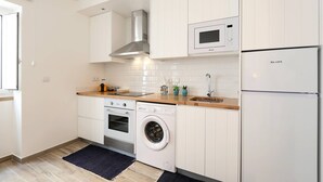 A compact kitchen with white cabinetry, a stainless steel range hood, a built-in oven, a microwave, a washing machine, and a refrigerator. - Sea & Sun Apartment II (Nazaré)
