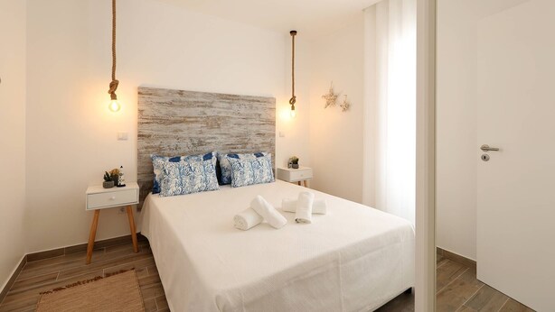 A bedroom with a wooden headboard, two bedside tables with lamps, a bed with white linens, and a door. - Sea & Sun Apartment II (Nazaré)