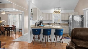 A modern kitchen with white cabinets, a stainless steel refrigerator, and a bar area with blue stools. - Ocean Peek in Ocean Dr.  6-bedroom/6.5 bath house in lovely North Myrtle Beach (North Myrtle Beach)
