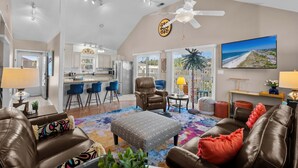A spacious living area with a brown leather sofa, a patterned ottoman, and a ceiling fan. - Ocean Peek in Ocean Dr.  6-bedroom/6.5 bath house in lovely North Myrtle Beach (North Myrtle Beach)