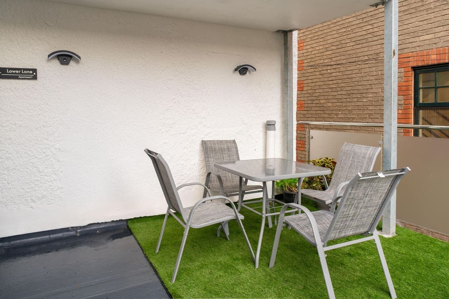 A patio with a table and four chairs, a small patch of artificial grass, and a brick wall.