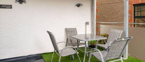 A patio with a table and four chairs, a small patch of artificial grass, and a brick wall.