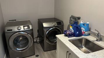 A laundry room with two front-loading washing machines, a sink with a marble countertop, and various cleaning supplies.