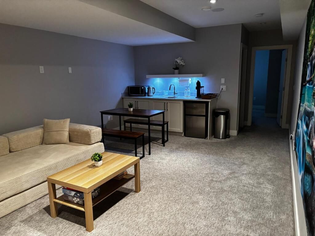 Un espace de vie compact comprenant un canapé, une table basse, un coin cuisine et une poubelle.