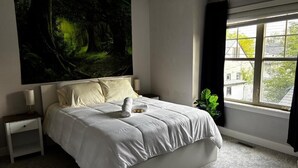 A bedroom with a large bed, a nightstand, a window with curtains, and a wall tapestry. - Nature Home near Downtown and 17th Av (Calgary)