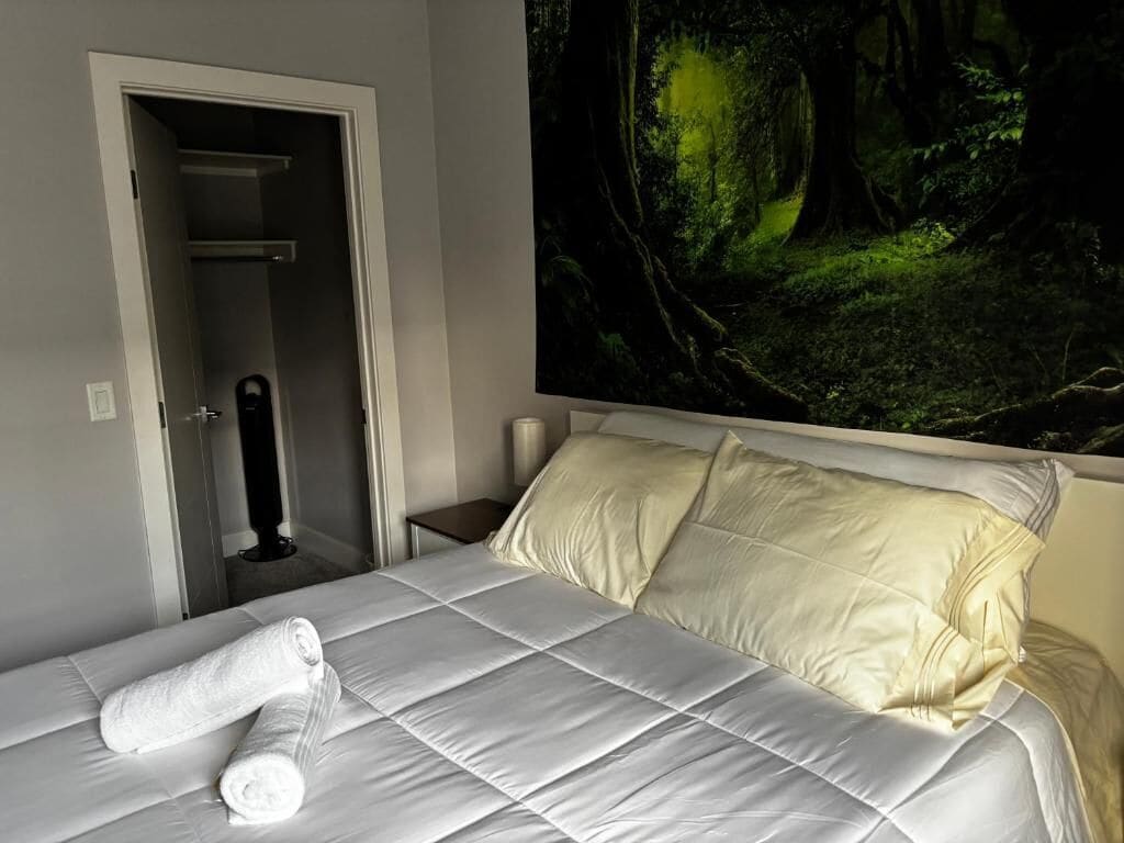 A hotel room with a bed, a door, and a large forest-themed painting on the wall.