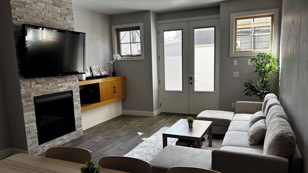 A modern living room with a fireplace, a flat-screen TV, a sofa, and a dining area. - Nature Home near Downtown and 17th Av (Calgary)