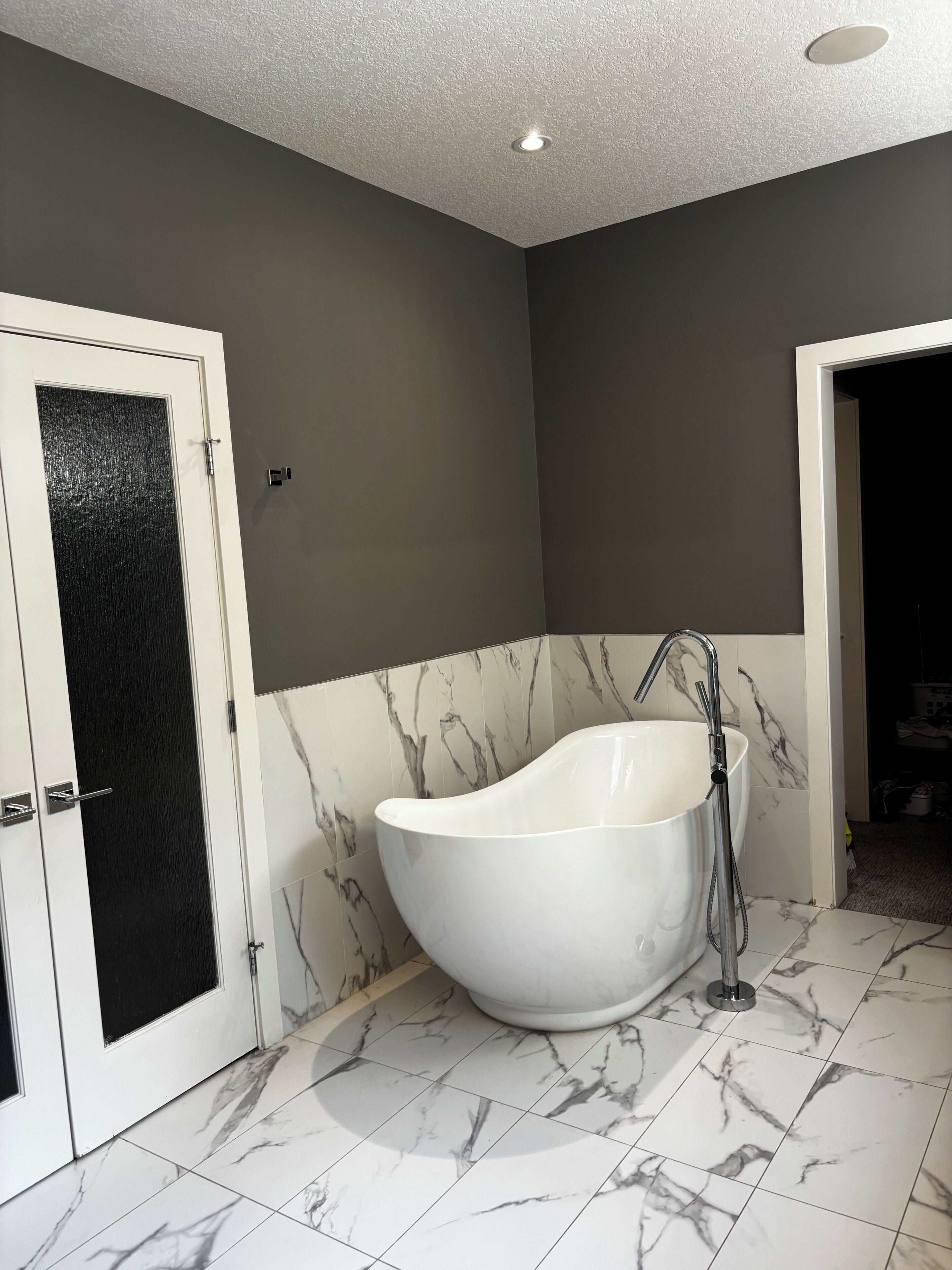 Une salle de bain avec une baignoire sur pieds, une porte avec un panneau noir, et des murs et un sol à motifs de marbre.