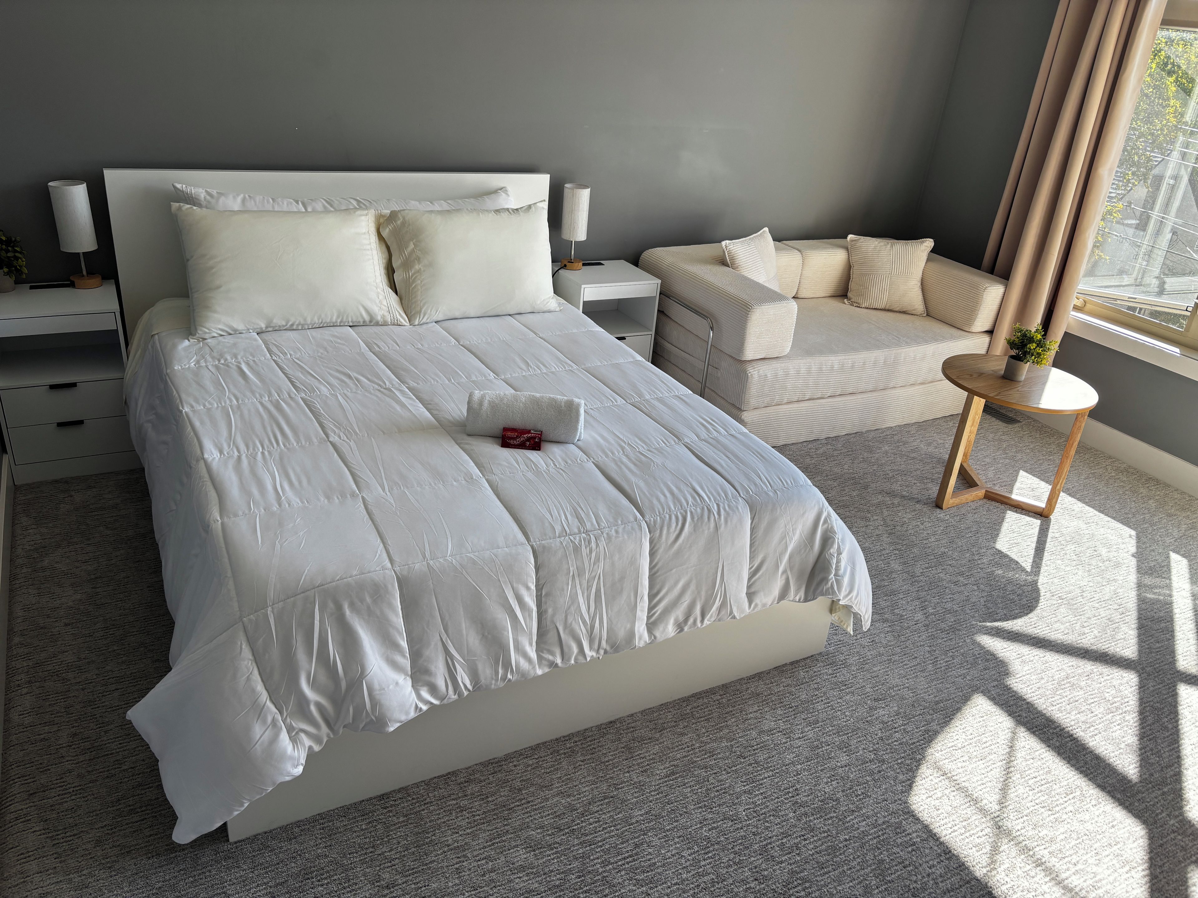 Un dormitorio moderno con una cama grande, una mesita de noche, una pequeña mesa redonda y un sofá.