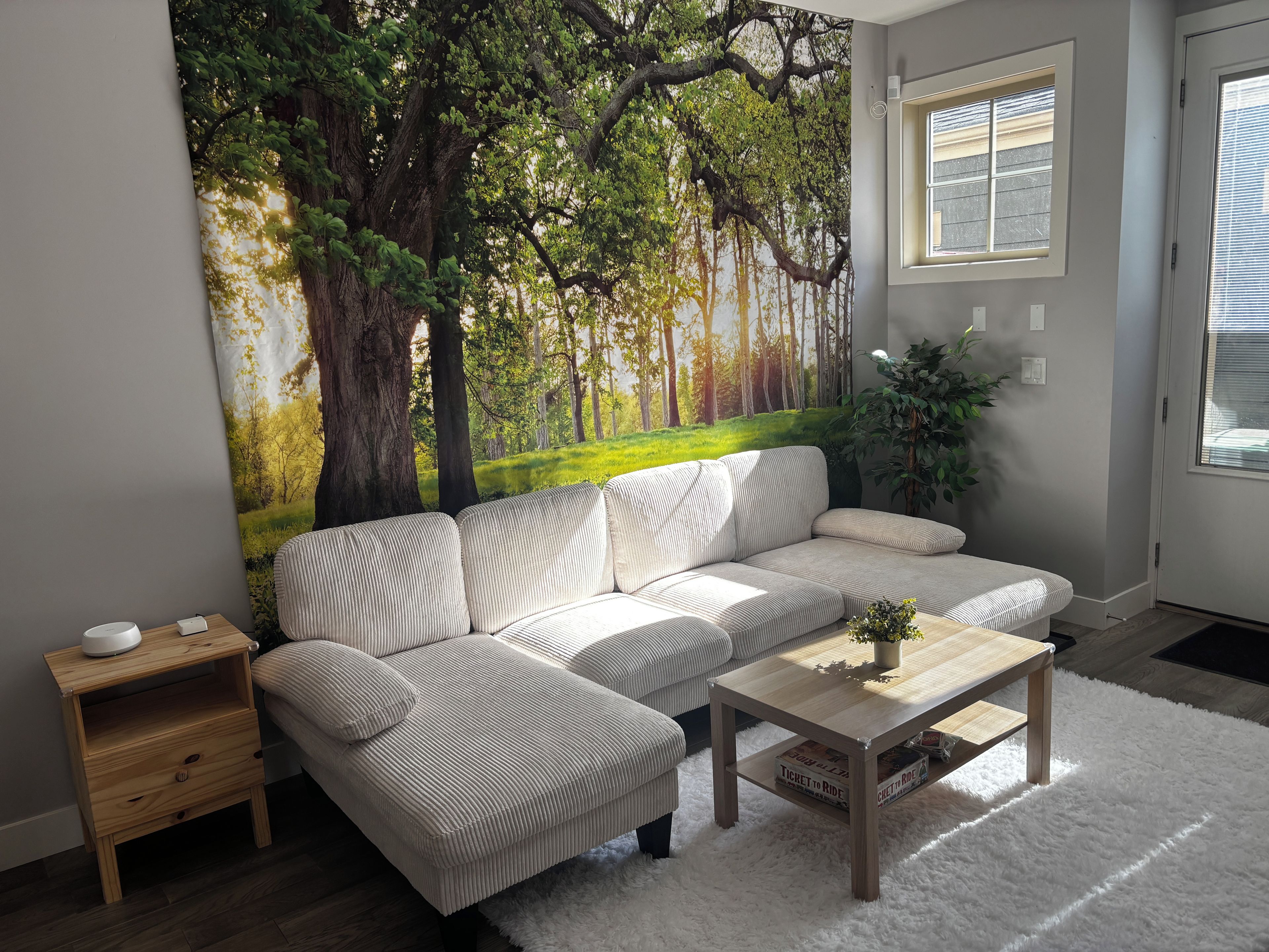 Un salon comprenant un canapé, une table basse, une table d’appoint et une grande fresque murale représentant une forêt.