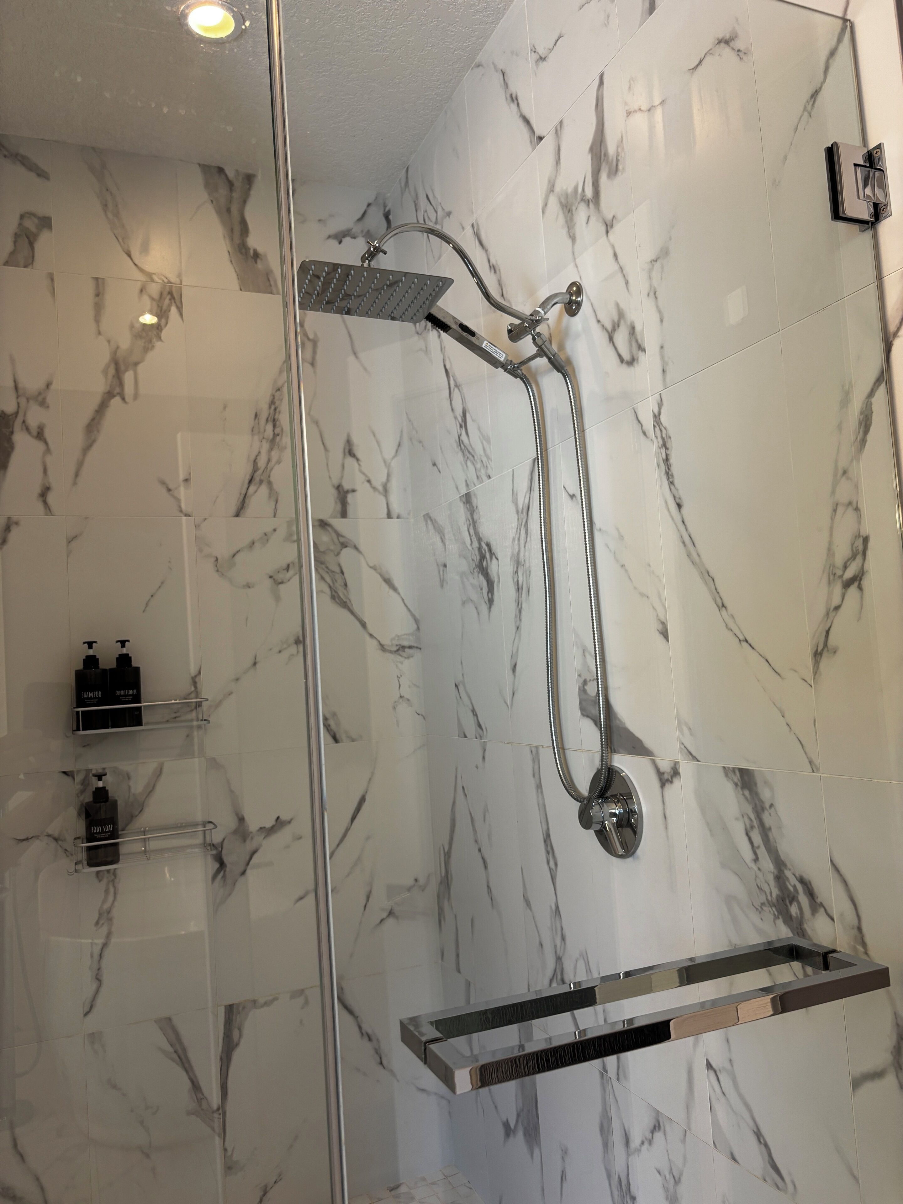 Une salle de bain moderne dotée d’une douche à parois de verre, de carreaux de marbre et d’une étagère intégrée pour les articles de toilette.