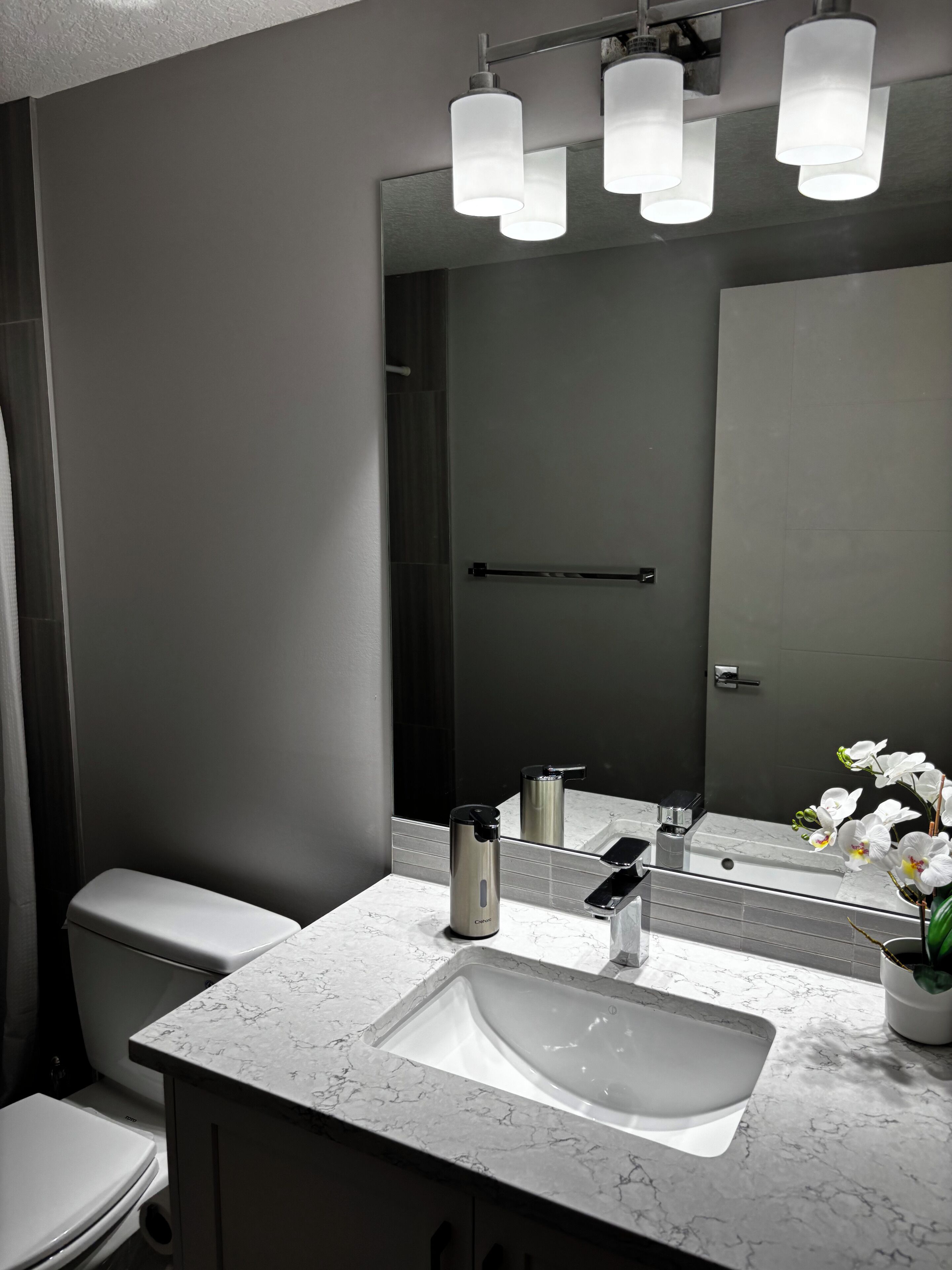 A modern bathroom with a white marble sink, a toilet, and a large mirror.