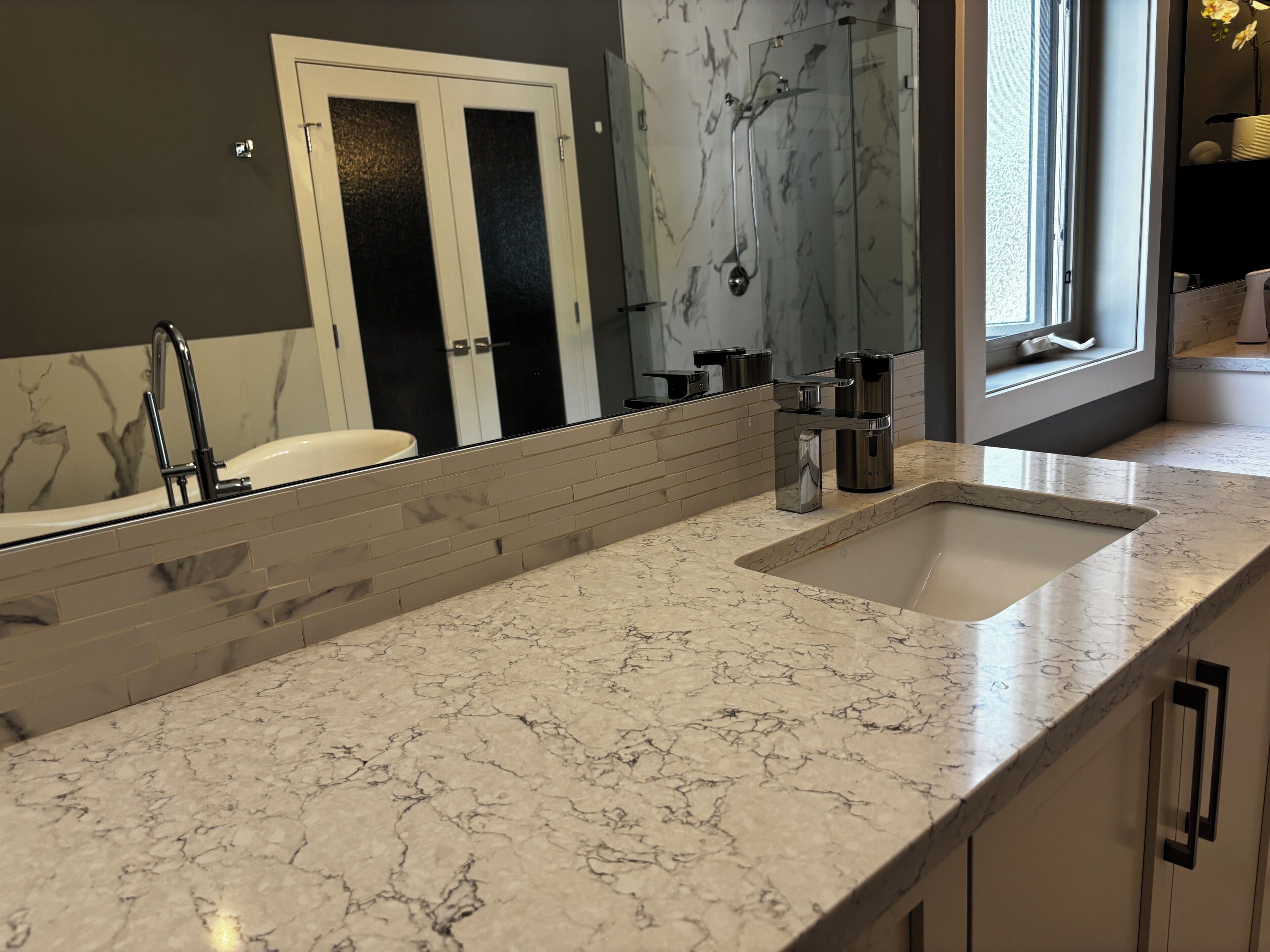 A bathroom with a large mirror, a sink, and a shower area.