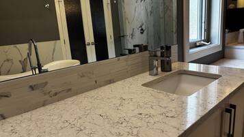 A bathroom with a large mirror, a sink, and a shower area.