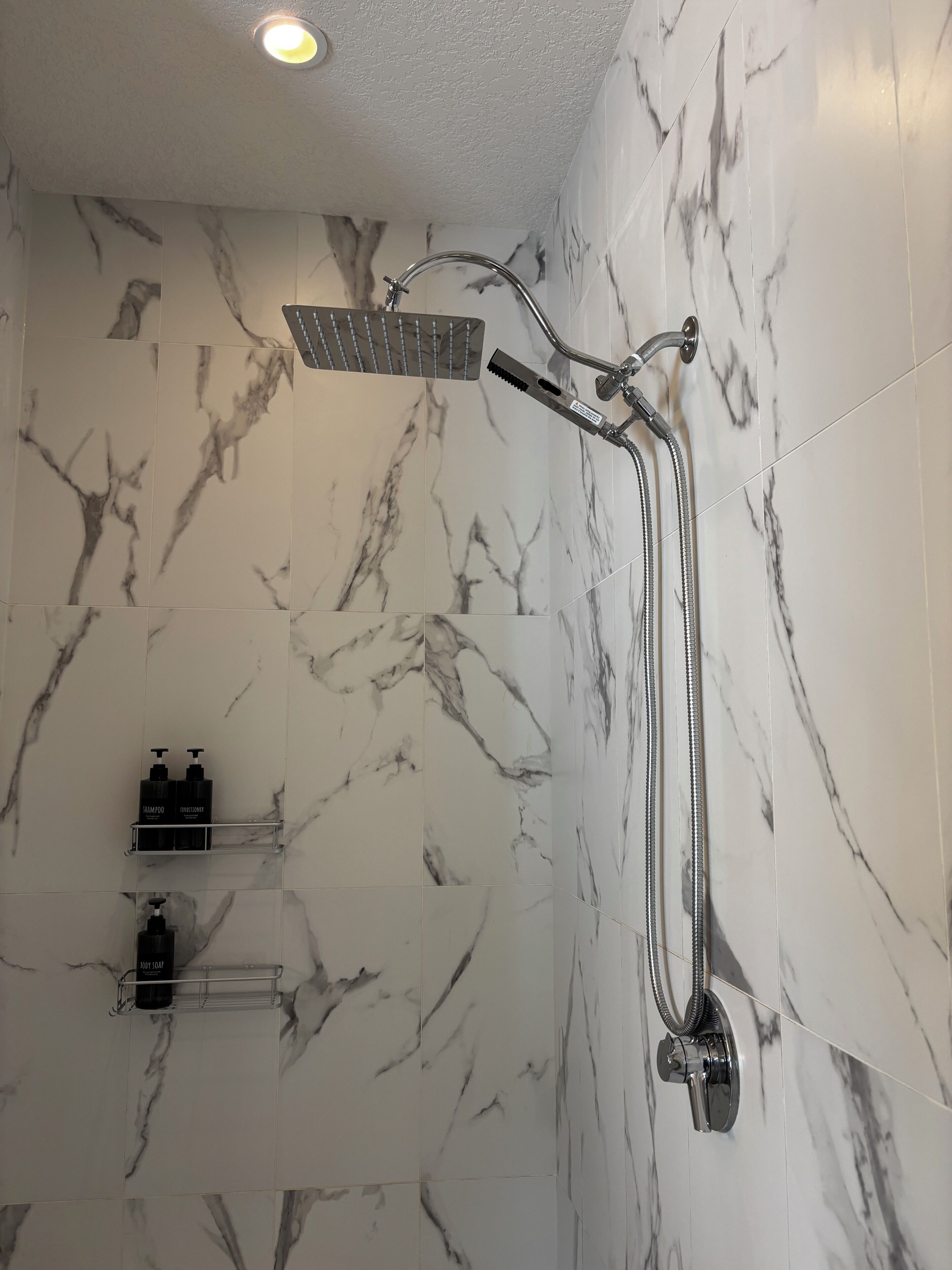 Un bagno con doccia, pareti in marmo e un ripiano con articoli da toilette.