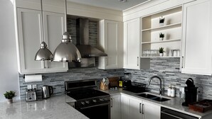 A modern kitchen with white cabinetry, a stainless steel range hood, a built-in oven, a sink, and a marble countertop. - Nature Home near Downtown and 17th Av (Calgary)