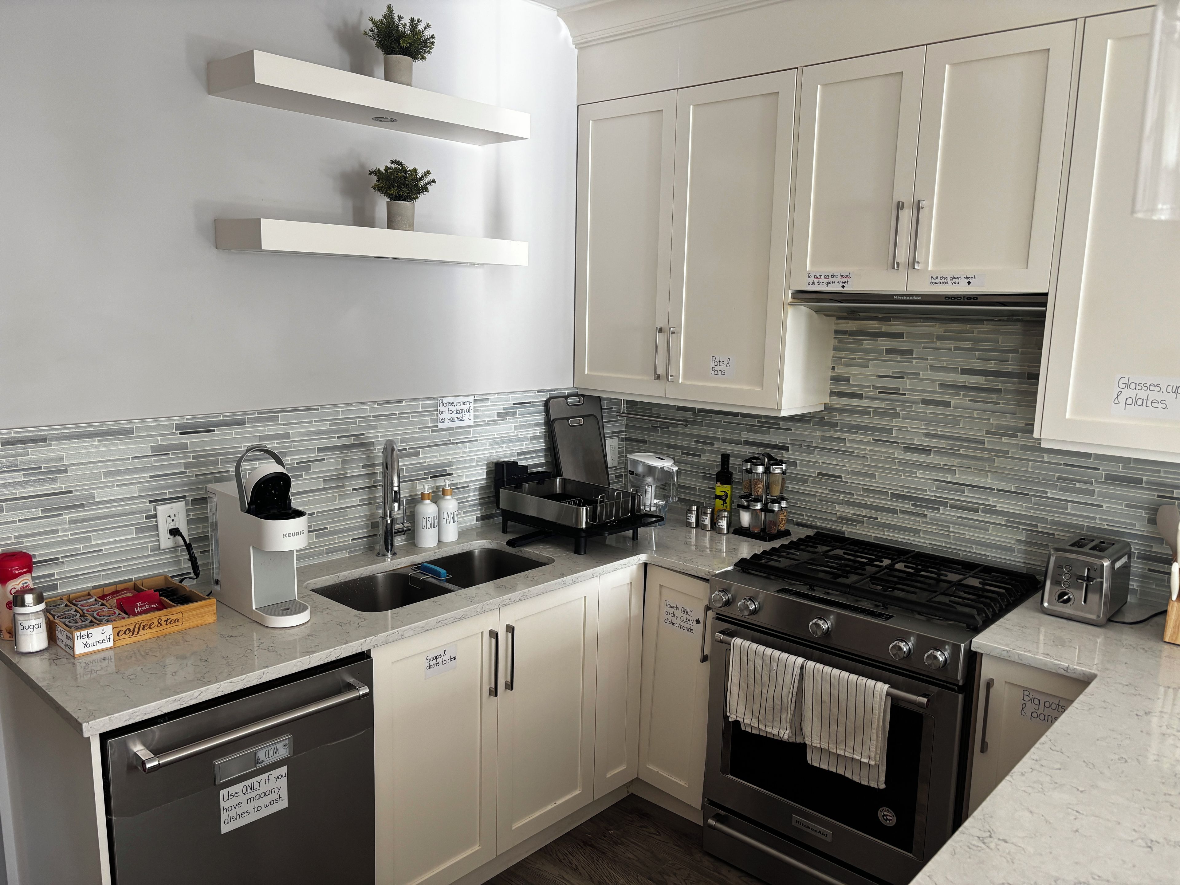 Una cocina moderna con armarios blancos, un lavavajillas de acero inoxidable, un horno empotrado y una cafetera.