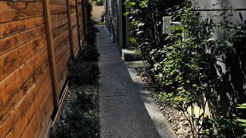Un sendero estrecho bordeado por vallas de madera y vegetación, que conduce a un edificio de aspecto oscuro.