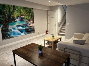 A living room with a large wall mural, a staircase, a sofa, a coffee table, and a small table with a plant.