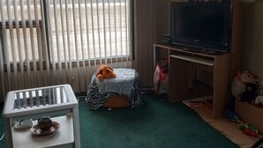 A room with a bed, a small table with a cup, a TV, and a teddy bear.