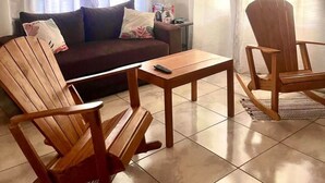 Una sala de estar con un sofá, dos sillas de madera, una mesita de centro y un televisor.