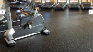 Et fitnessrum med flere løbebånd og en motionscykel, store vinduer med udsigt til grønne områder, og en loftsvifte.
