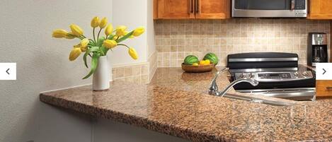 A kitchen with granite countertops, a stainless steel microwave, a gas stove, and wooden cabinets.