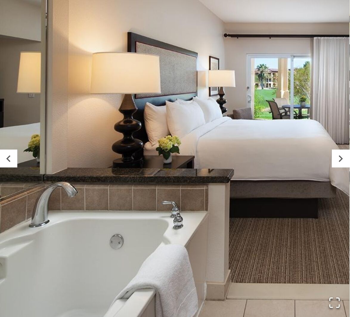 Une chambre d’hôtel avec un grand lit, une salle de bain séparée avec une baignoire et une vue sur un espace paysager aménagé.
