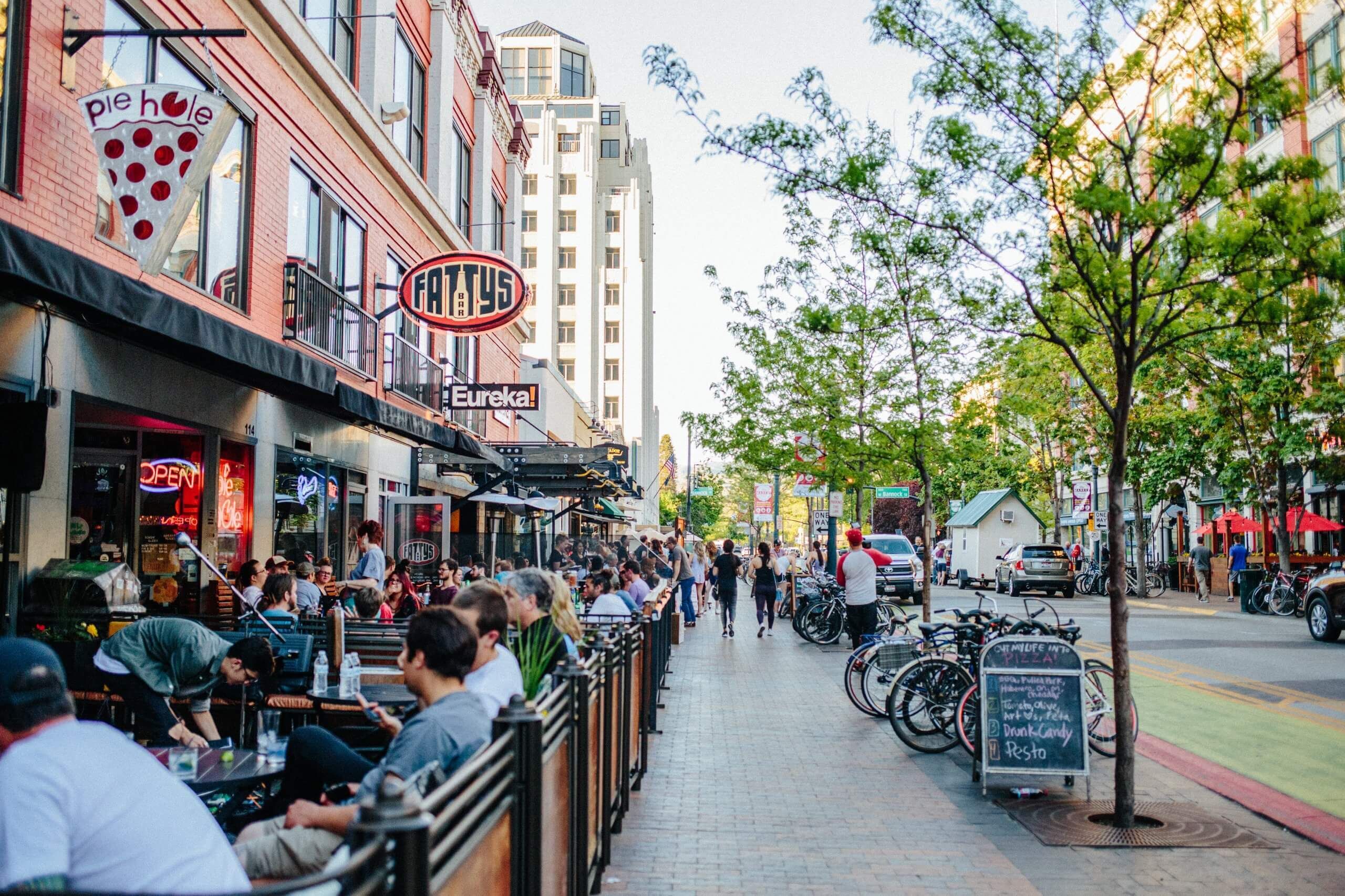 Una calle urbana concurrida con terrazas en diversos cafés y restaurantes.