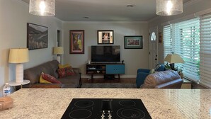 A living room with a TV, two pendant lights, a fireplace, and a kitchen area with a stove. - Charming Masters Cottage within a short walk <1 mile to the Augusta National. (Augusta)
