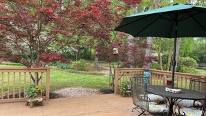 A wooden deck with a table and chairs, surrounded by a wooden fence and trees with red leaves. - Charming Masters Cottage within a short walk <1 mile to the Augusta National. (Augusta)