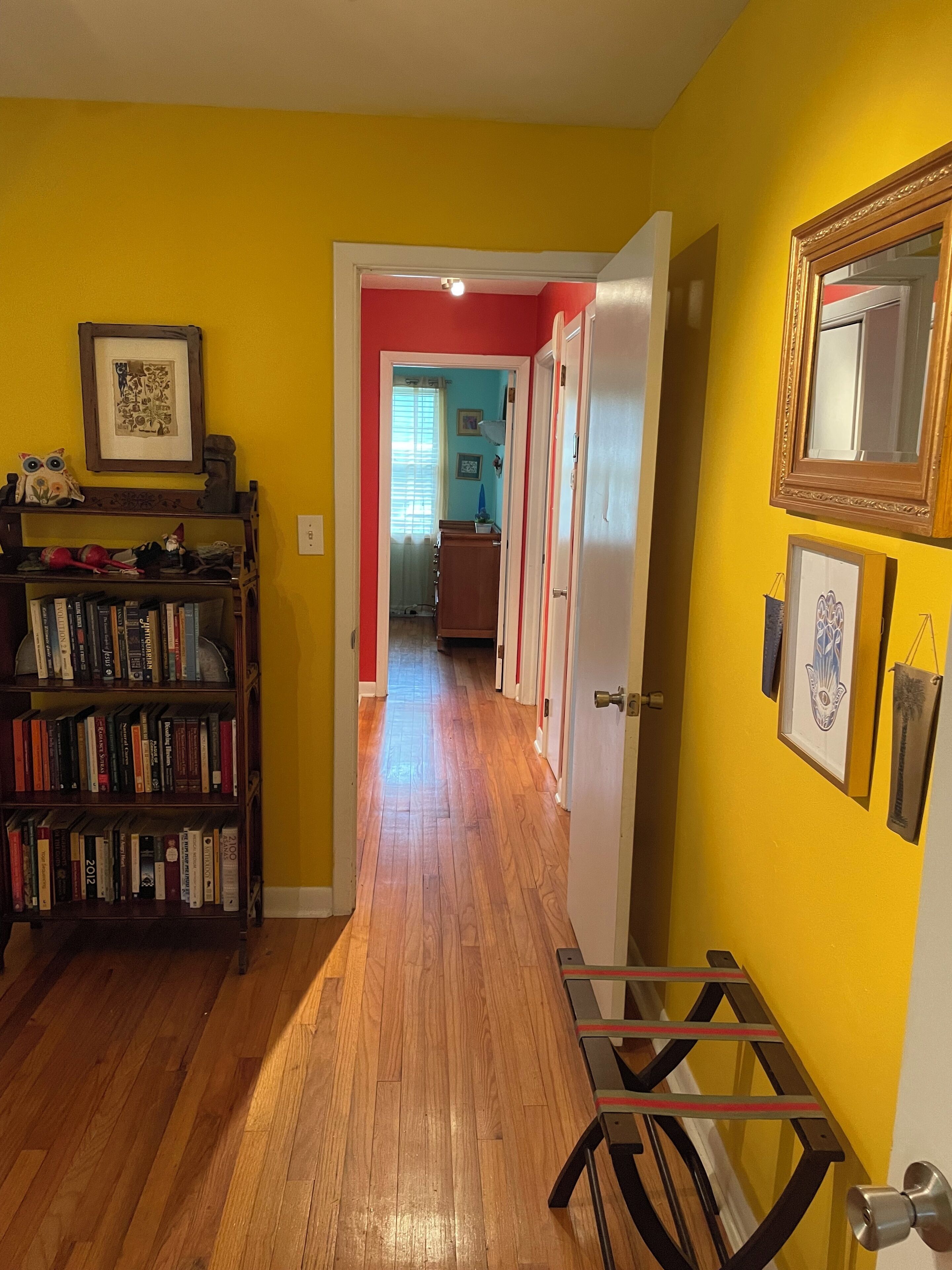 Un pasillo con suelo de madera, una estantería y una puerta que da a otra habitación.
