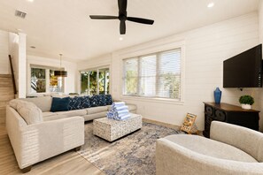 Ein Wohnzimmer mit einer Couch, Sesseln, einem Couchtisch, einem Fernseher und einem Deckenventilator.