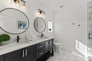 Une salle de bain moderne aux couleurs blanc et noir, comprenant un grand miroir, deux lavabos, des toilettes et un espace douche.