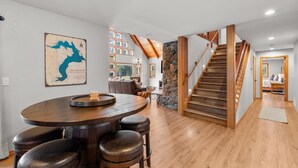 A spacious dining area with a wooden table and bar stools, a stone accent wall, and a staircase leading to another level. - Bottle Bay View Lodge – 21-Acre Lakefront Retreat (Sagle)