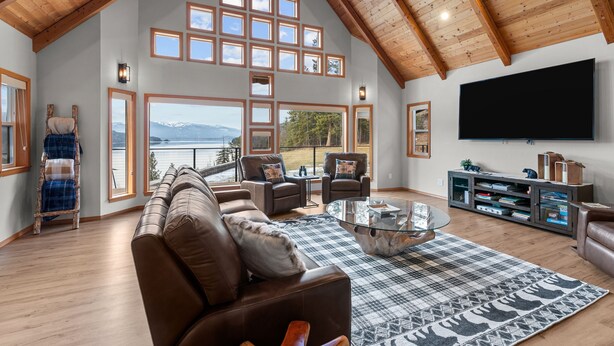 A spacious living room with a high ceiling, large windows, a fireplace, and a flat-screen TV. - Bottle Bay View Lodge – 21-Acre Lakefront Retreat (Sagle)